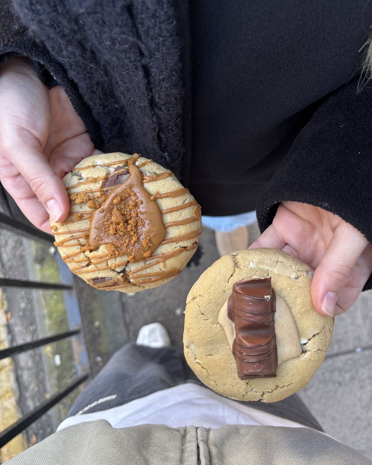 Twee grote cookies met karamel en chocolade, vastgehouden boven de stoep