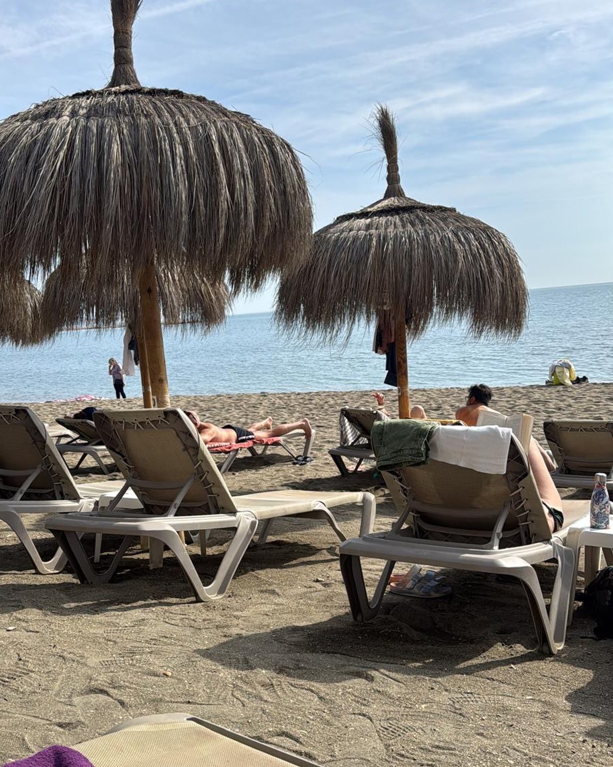 Strandbedjes onder rieten parasols op Playa de la Malagueta, met de zee op de achtergrond
