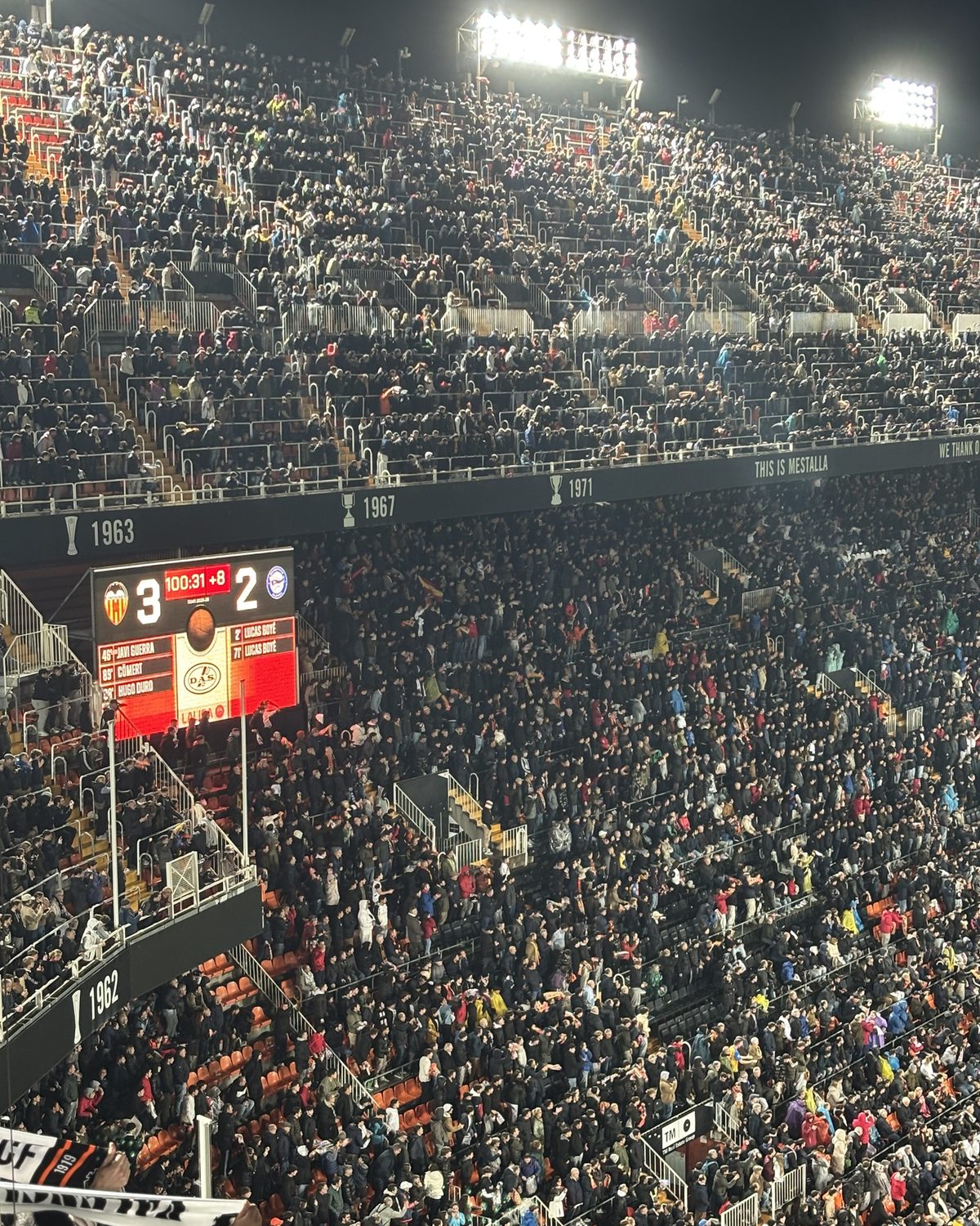 Een volle tribune in het Mestalla-stadion van Valencia CF bij avond, met het scorebord op 3-2